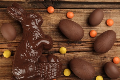 Photo of Chocolate Easter bunny, candies and eggs on wooden table, flat lay