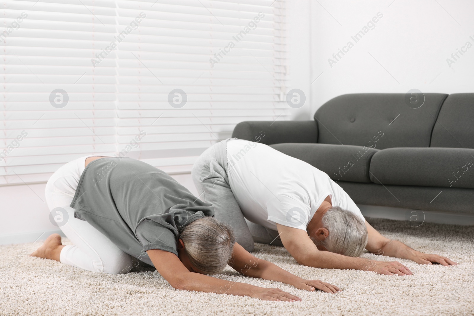 Photo of Senior couple practicing yoga on carpet at home. Healthy lifestyle