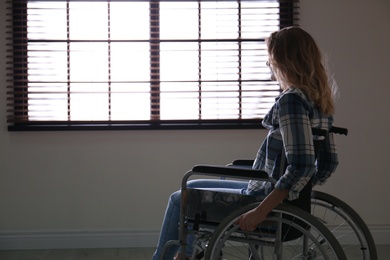 Young woman in wheelchair near window indoors