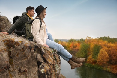 Couple of hikers sitting on steep cliff near mountain river