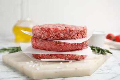Photo of Raw hamburger patties with rosemary and salt on white marble table, closeup
