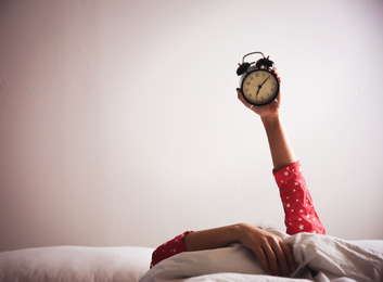 Closeup view of woman with alarm clock lying in bed, space for text. Morning time