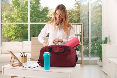 Businesswoman packing sports stuff for training into bag in office