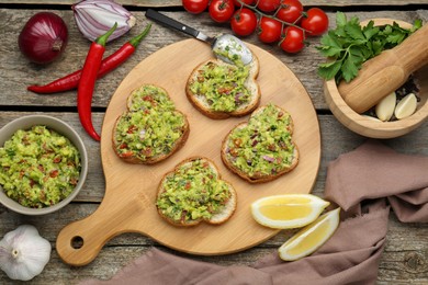 Photo of Slices of bread with tasty guacamole and ingredients on wooden table, flat lay