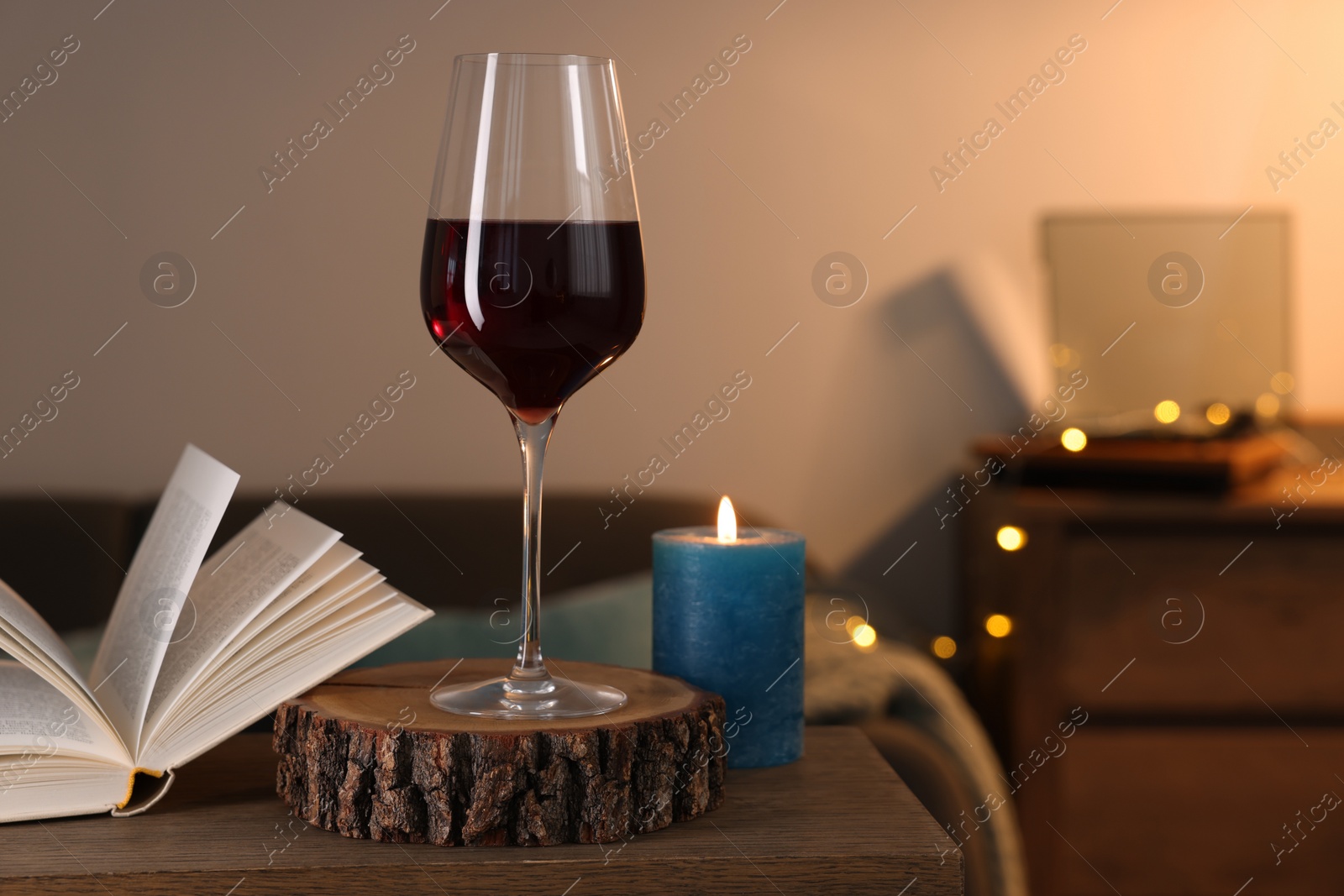 Photo of Glass of red wine, open book and burning candle on wooden table in room, space for text. Relax at home