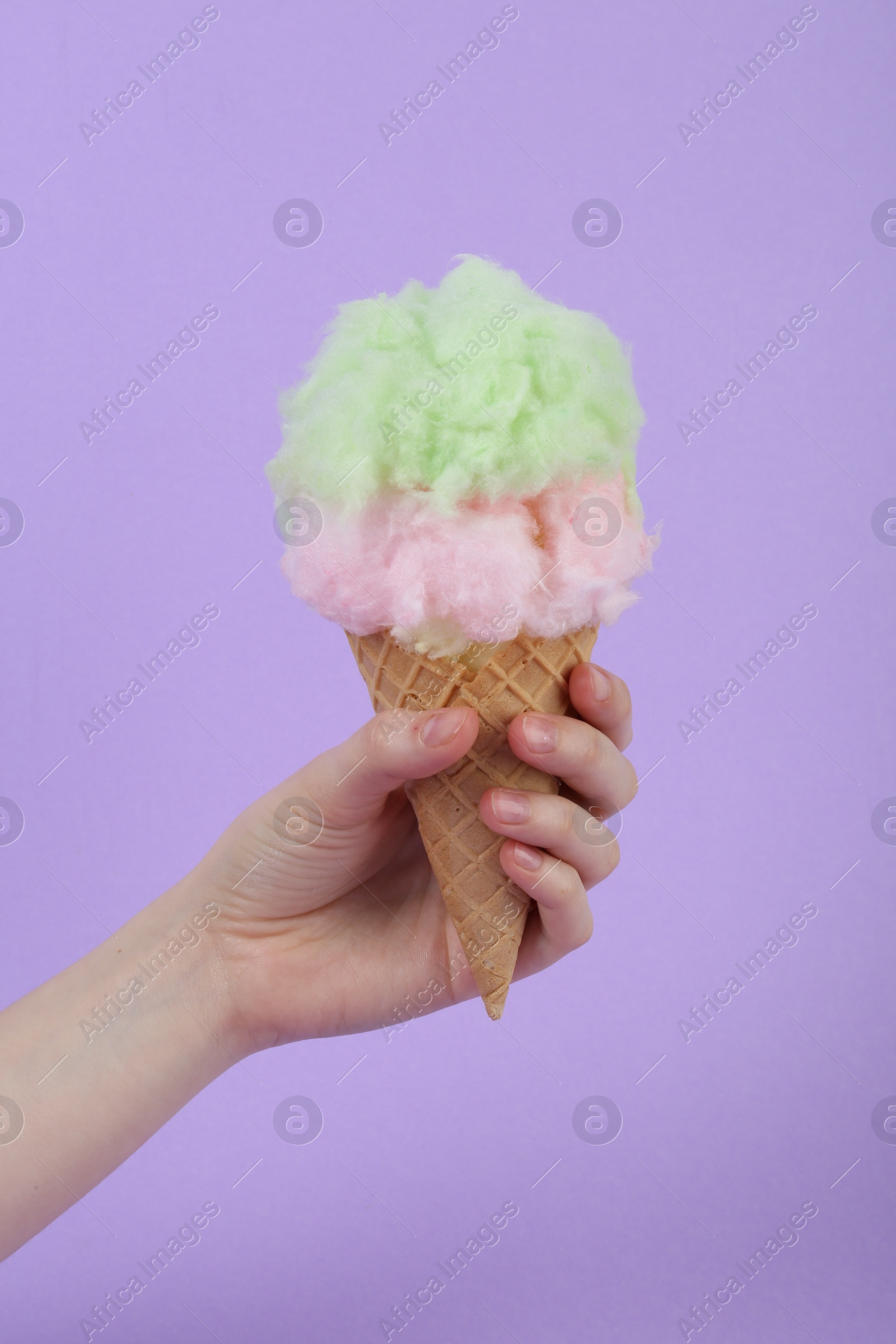 Photo of Woman holding waffle cone with cotton candy on violet background, closeup