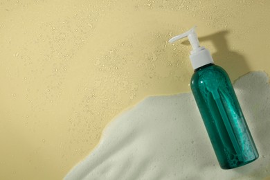 Photo of Bottle of face cleanser and white foam on beige background, top view with space for text. Skin care cosmetic