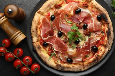 Photo of Tasty pizza with cured ham, olives, tomatoes and parsley on black table, top view