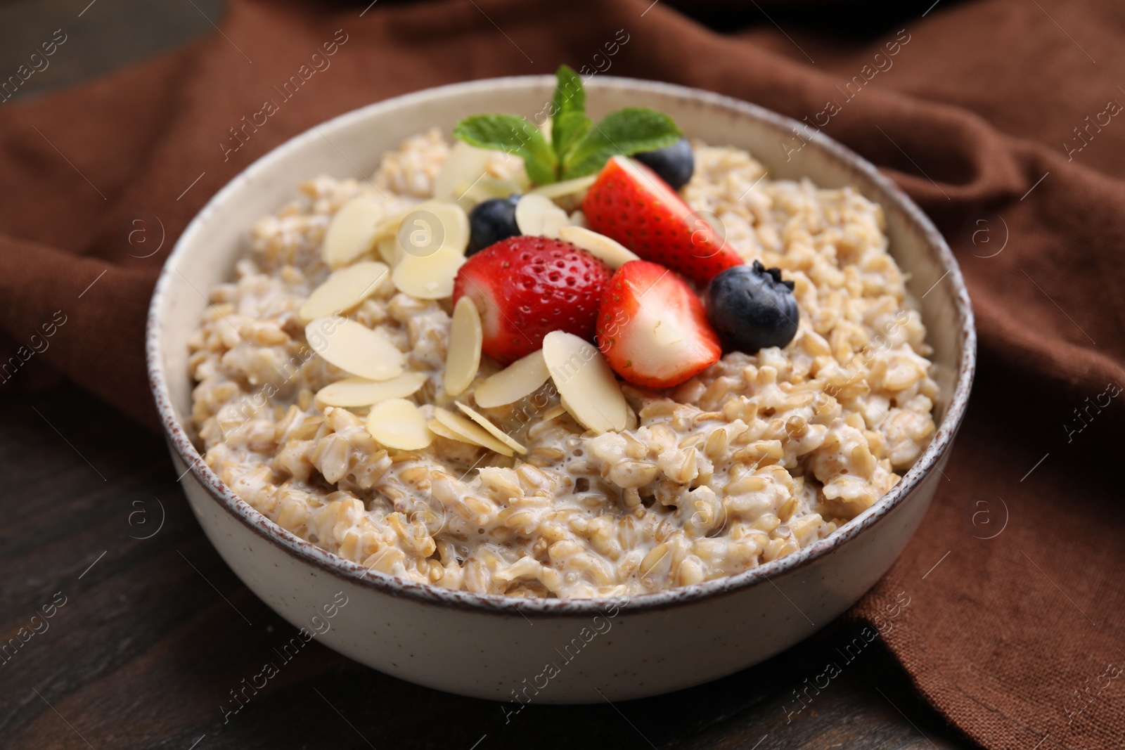 Photo of Tasty oatmeal with strawberries, blueberries and almond flakes in bowl on wooden table, closeup