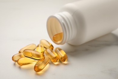 Photo of Overturned bottle with dietary supplement capsules on white table, closeup