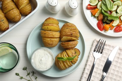 Photo of Delicious homemade Hasselback potatoes served on white wooden table, flat lay