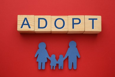 Photo of Family figure and word Adopt made of cubes on red background, flat lay