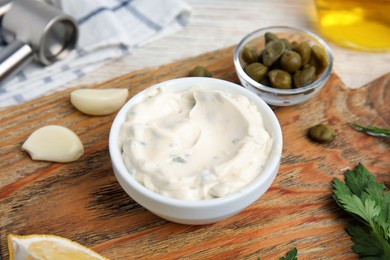 Photo of Tasty tartar sauce and ingredients on wooden board