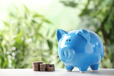 Piggy bank and coins on table against blurred background. Space for text