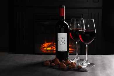 Photo of Red wine and chocolate truffles on gray table against fireplace, space for text