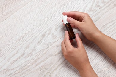 Woman with bottle of essential oil on wooden background, top view and space for text