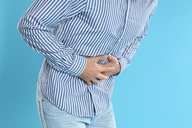 Photo of Man suffering from stomach ache on light blue background, closeup. Food poisoning