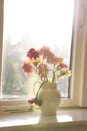 Photo of Jug with beautiful gerbera flowers on windowsill