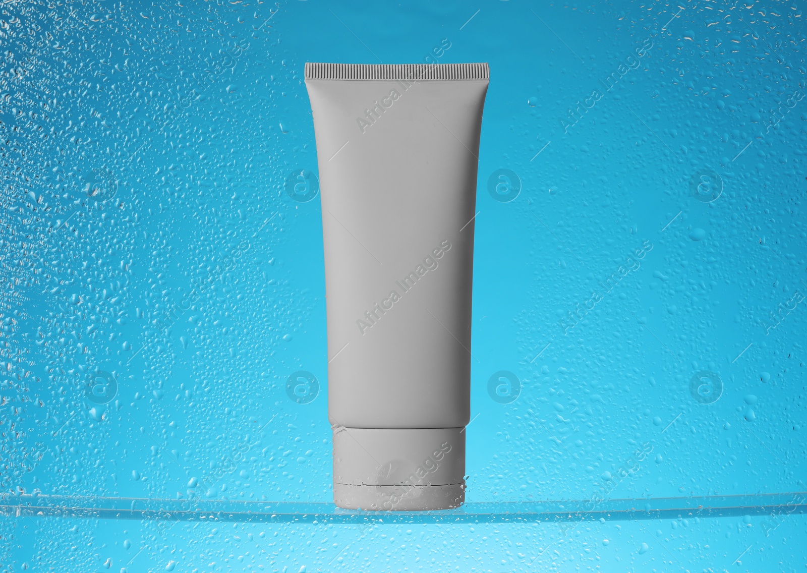 Photo of Tube with moisturizing cream on light blue background, view through wet glass