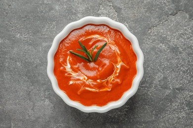 Bowl with fresh homemade tomato soup on grey background, top view