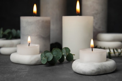 Photo of Composition with burning candles, spa stones and eucalyptus on grey table