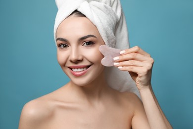 Photo of Beautiful young woman doing facial massage with gua sha tool on blue background