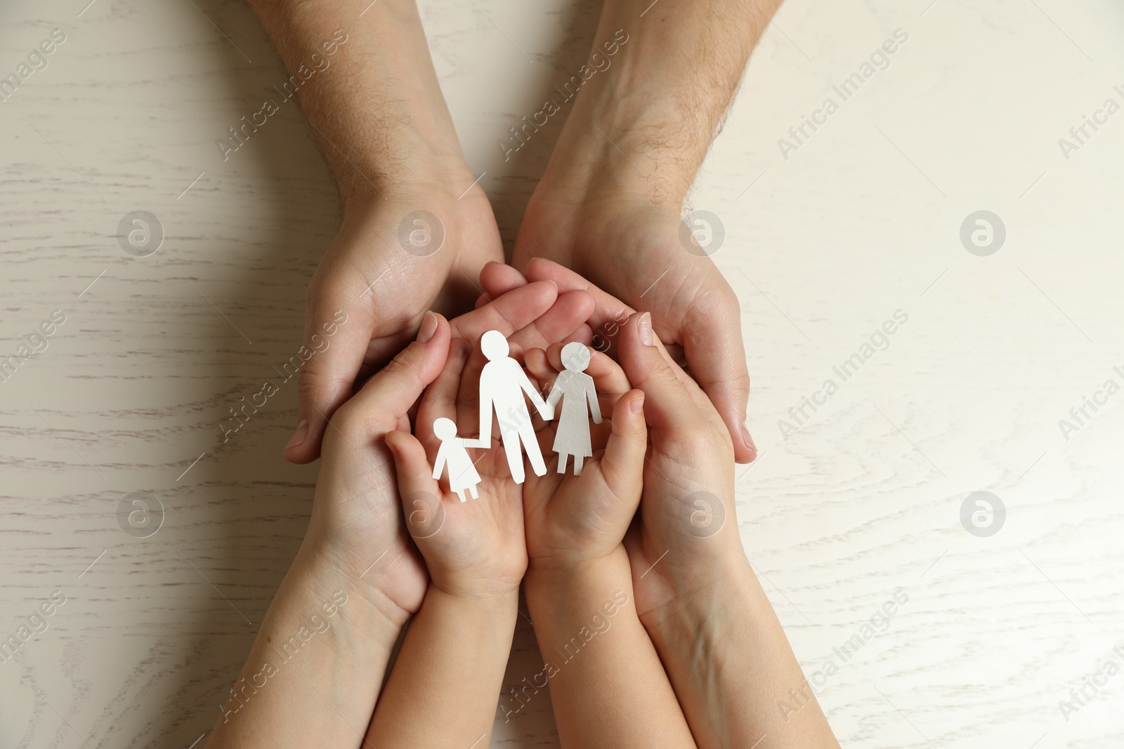 Photo of Parents and child holding paper cutout of family at white wooden table, top view