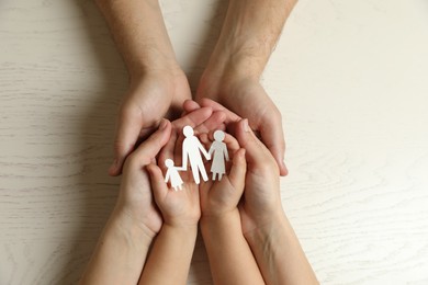 Photo of Parents and child holding paper cutout of family at white wooden table, top view