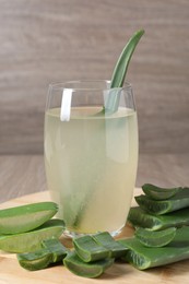 Photo of Tasty aloe juice in glass and cut fresh leaves on wooden table, closeup