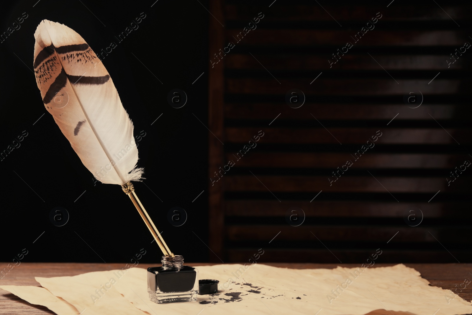 Photo of Inkwell with feather pen and vintage parchment with ink stains on wooden table indoors. Space for text