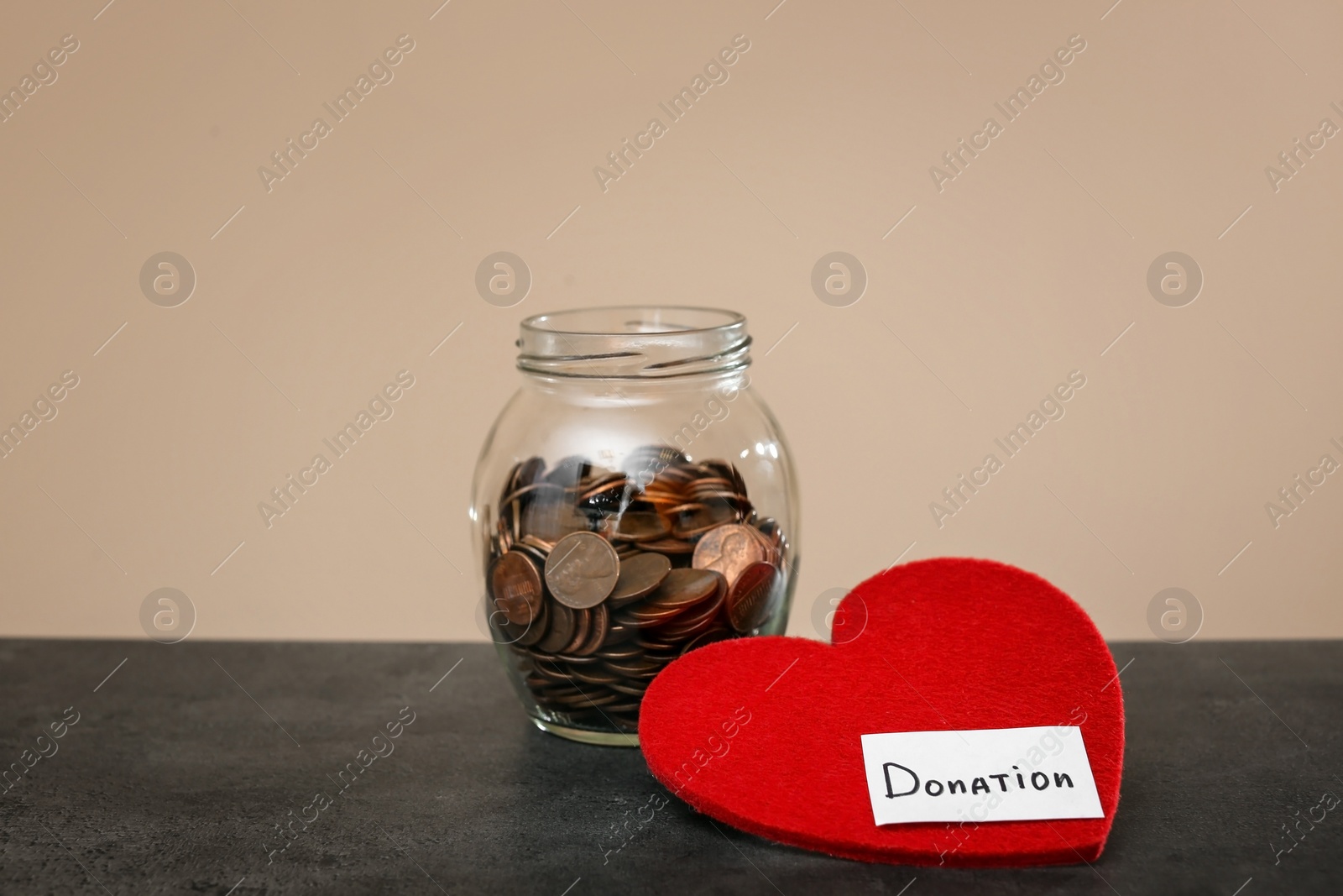 Photo of Donation jar with coins and red heart on table against color background