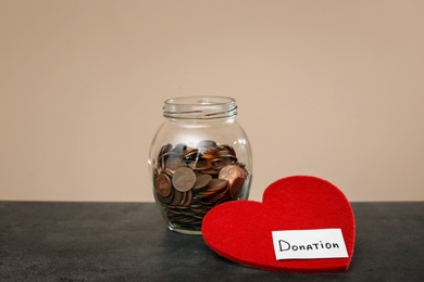 Photo of Donation jar with coins and red heart on table against color background