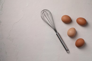 Photo of Metal whisk and raw eggs on light table, flat lay. Space for text