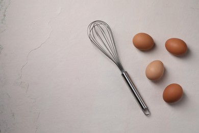 Metal whisk and raw eggs on light table, flat lay. Space for text