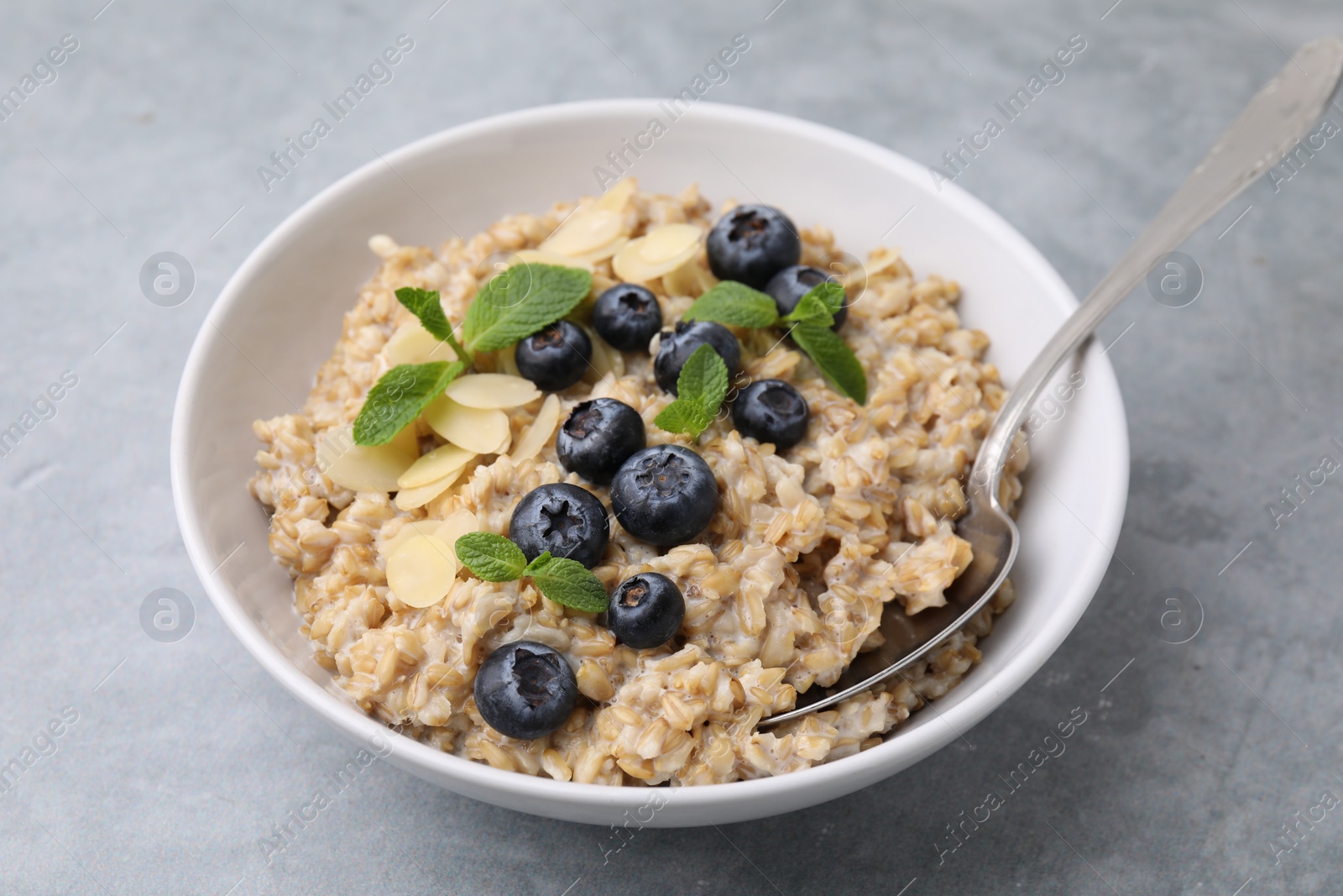 Photo of Tasty oatmeal with blueberries, mint and almond petals in bowl on grey table, closeup