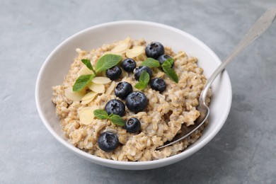 Photo of Tasty oatmeal with blueberries, mint and almond petals in bowl on grey table, closeup