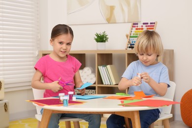 Girl with scissors and boy using glue stick at desk in room. Home workplace