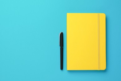 Photo of Yellow notebook and pen on turquoise background, flat lay. Space for text