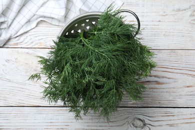 Photo of Fresh dill in colander on white wooden table, top view