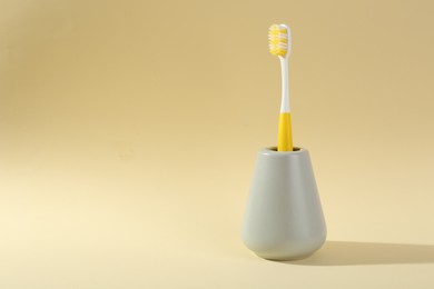 Photo of Plastic toothbrush in holder on pale yellow background, space for text