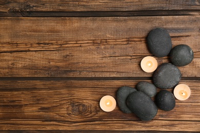 Photo of Spa stones and lit candles on wooden background, flat lay with space for text