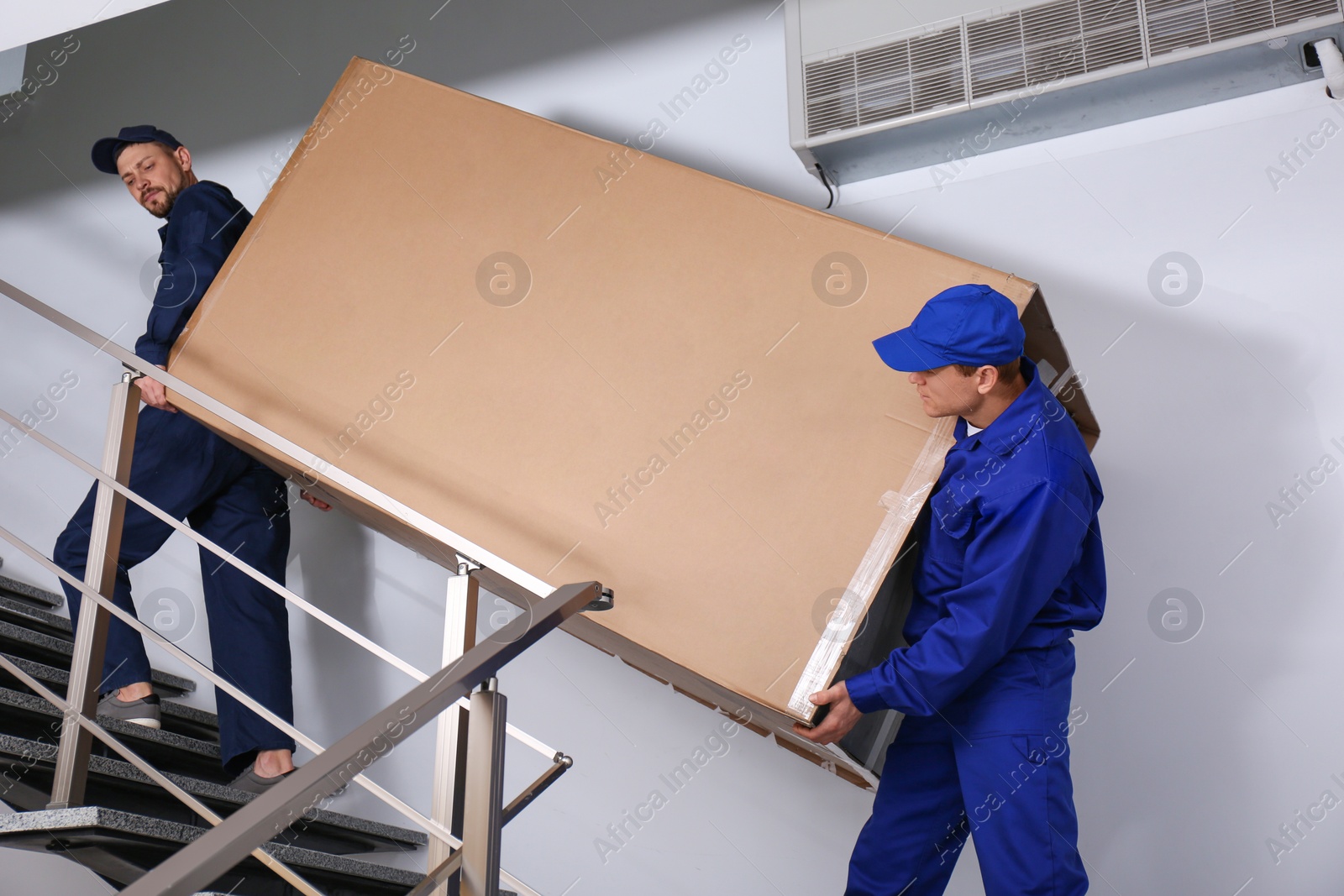 Photo of Professional workers carrying refrigerator on stairs indoors