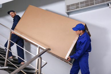 Professional workers carrying refrigerator on stairs indoors