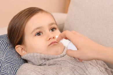Photo of Mother using nasal spray to treat her little daughter on sofa, closeup