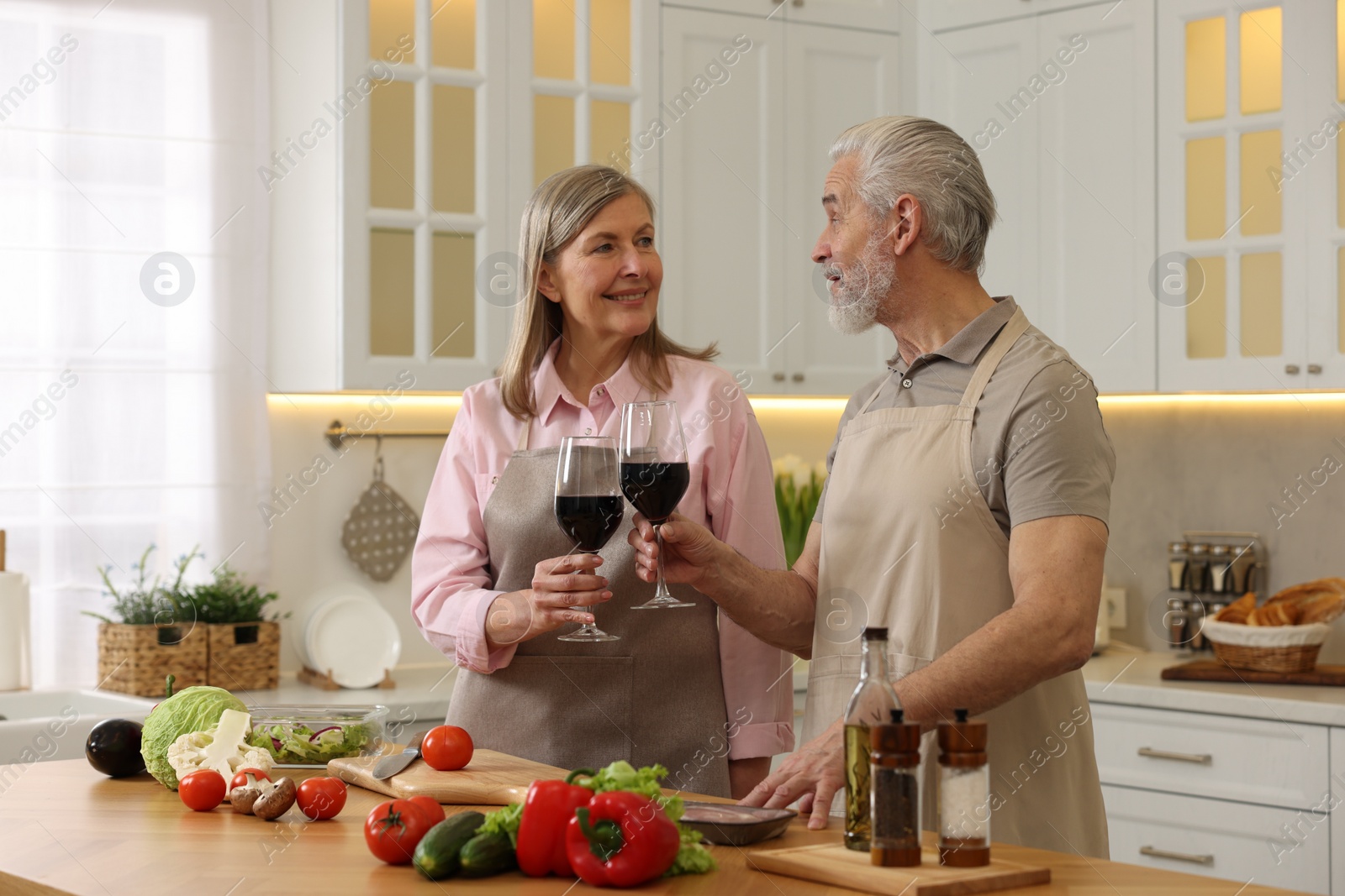 Photo of Happy senior couple with glasses of wine cooking together in kitchen