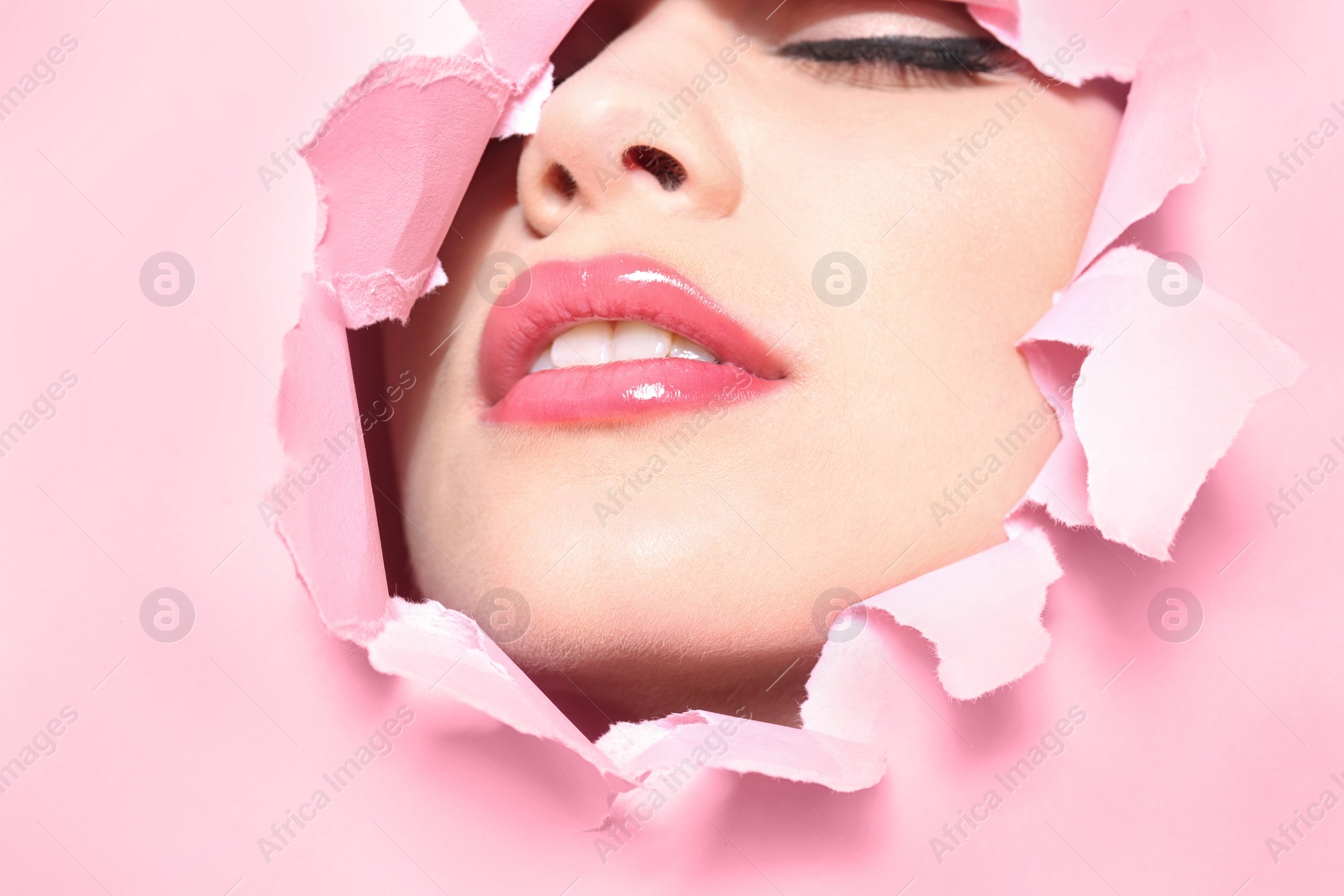 Photo of View of beautiful young woman with perfect lips makeup through hole in color paper