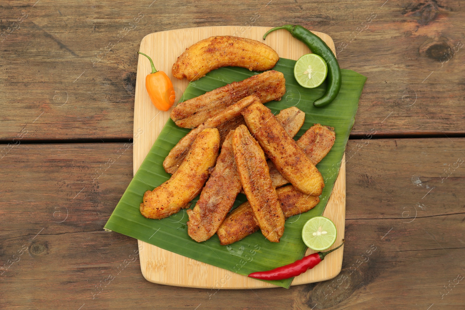 Photo of Delicious fried bananas, different peppers and cut limes on wooden table, flat lay