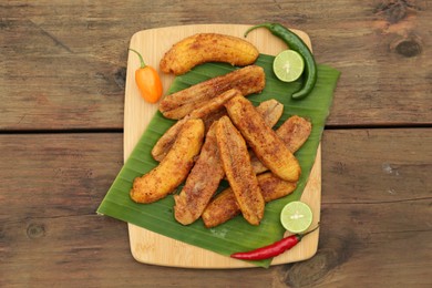 Delicious fried bananas, different peppers and cut limes on wooden table, flat lay