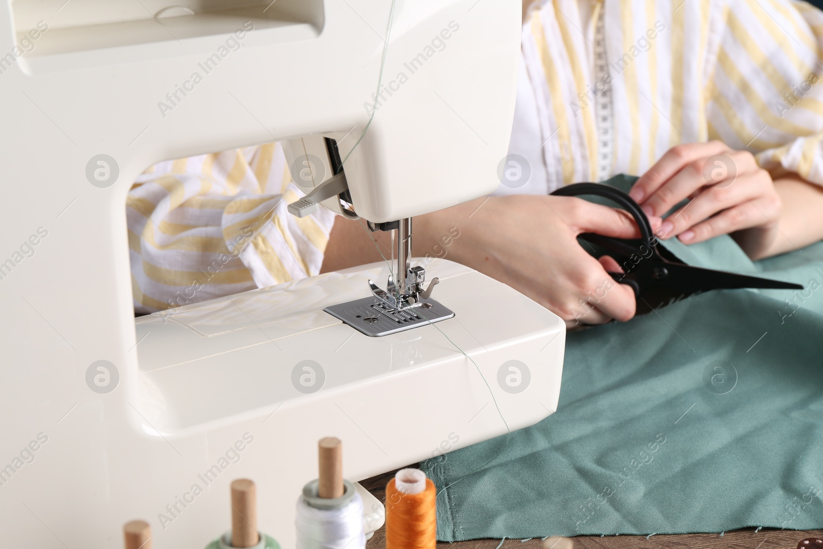 Photo of Seamstress cutting fabric at table indoors, closeup