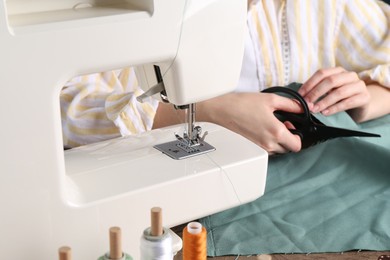 Photo of Seamstress cutting fabric at table indoors, closeup